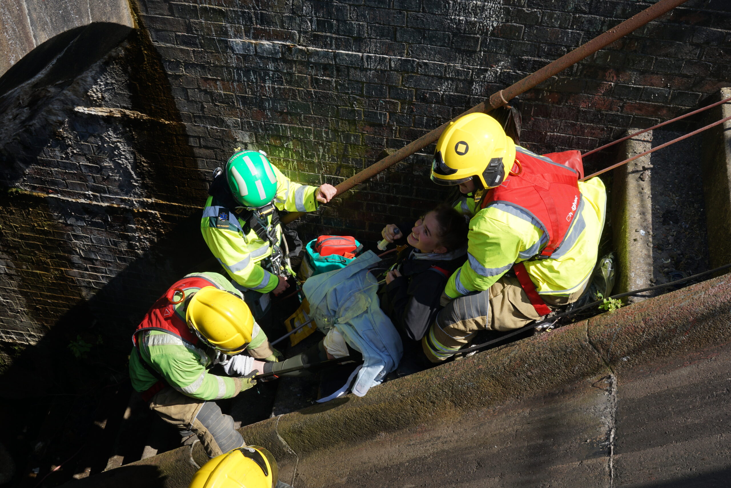 A group of firefighters wait at the top of a decline to help pull two injured patients from a hole.