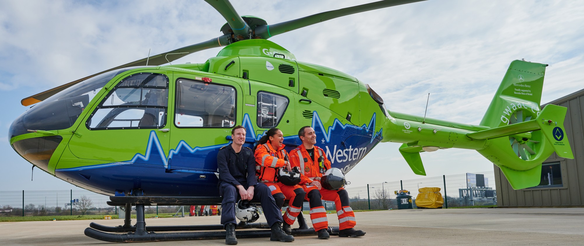 Three crew members sitting on the side of the helicopter.