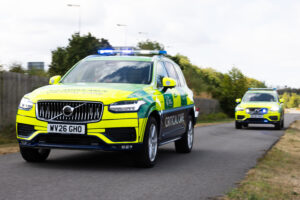 Two Great Western Air Ambulance Charity Volvo critical care cars driving along a tarmac road with their blue emergency lights flashing