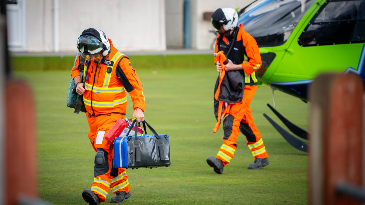 Two members of the GWAAC crew head from the green and blue helicopter with medical kit