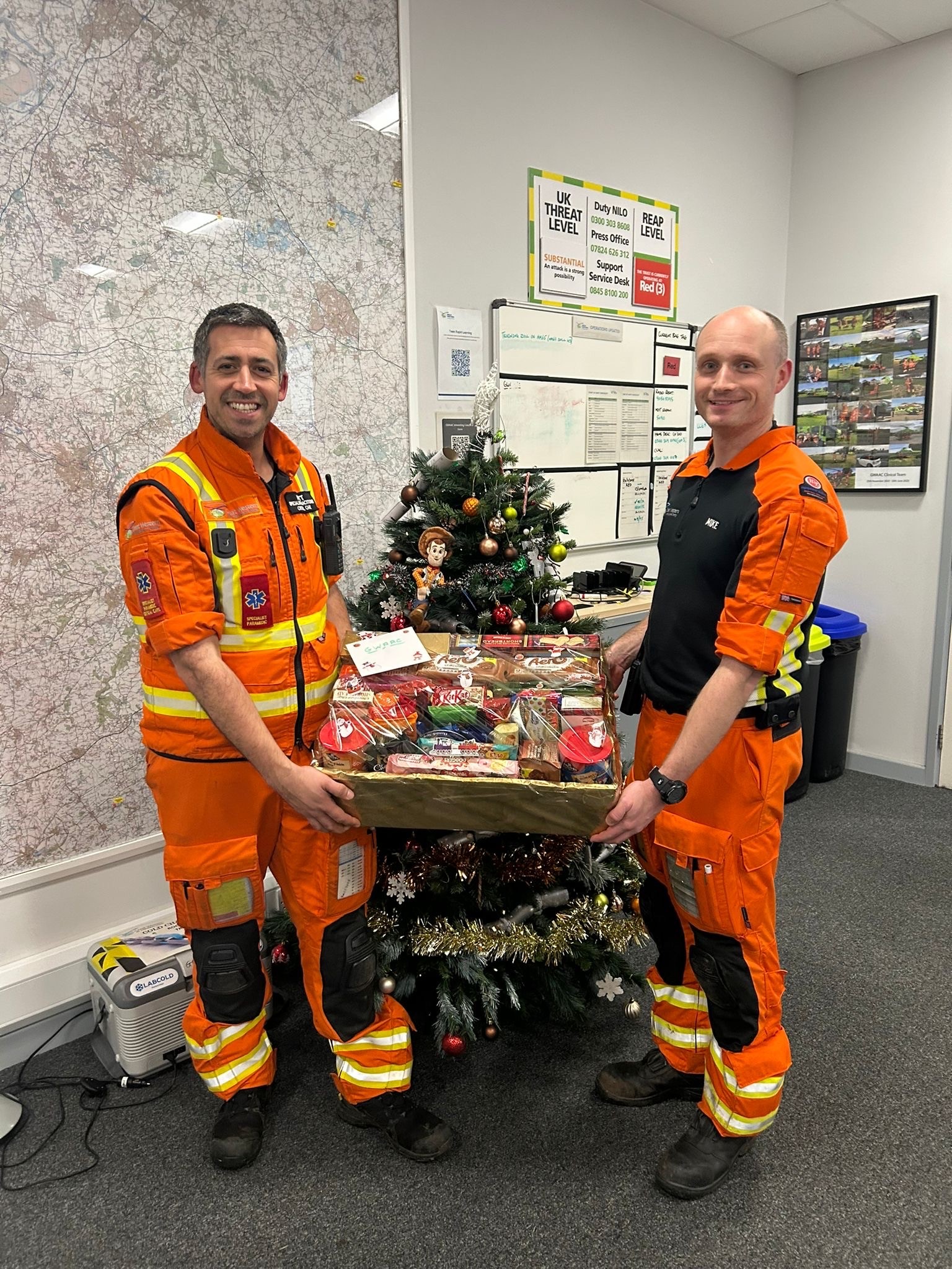 GWAAC crew, dressed in orange, post with a large hamper in front of a Christmas tree in the GWAAC airbase