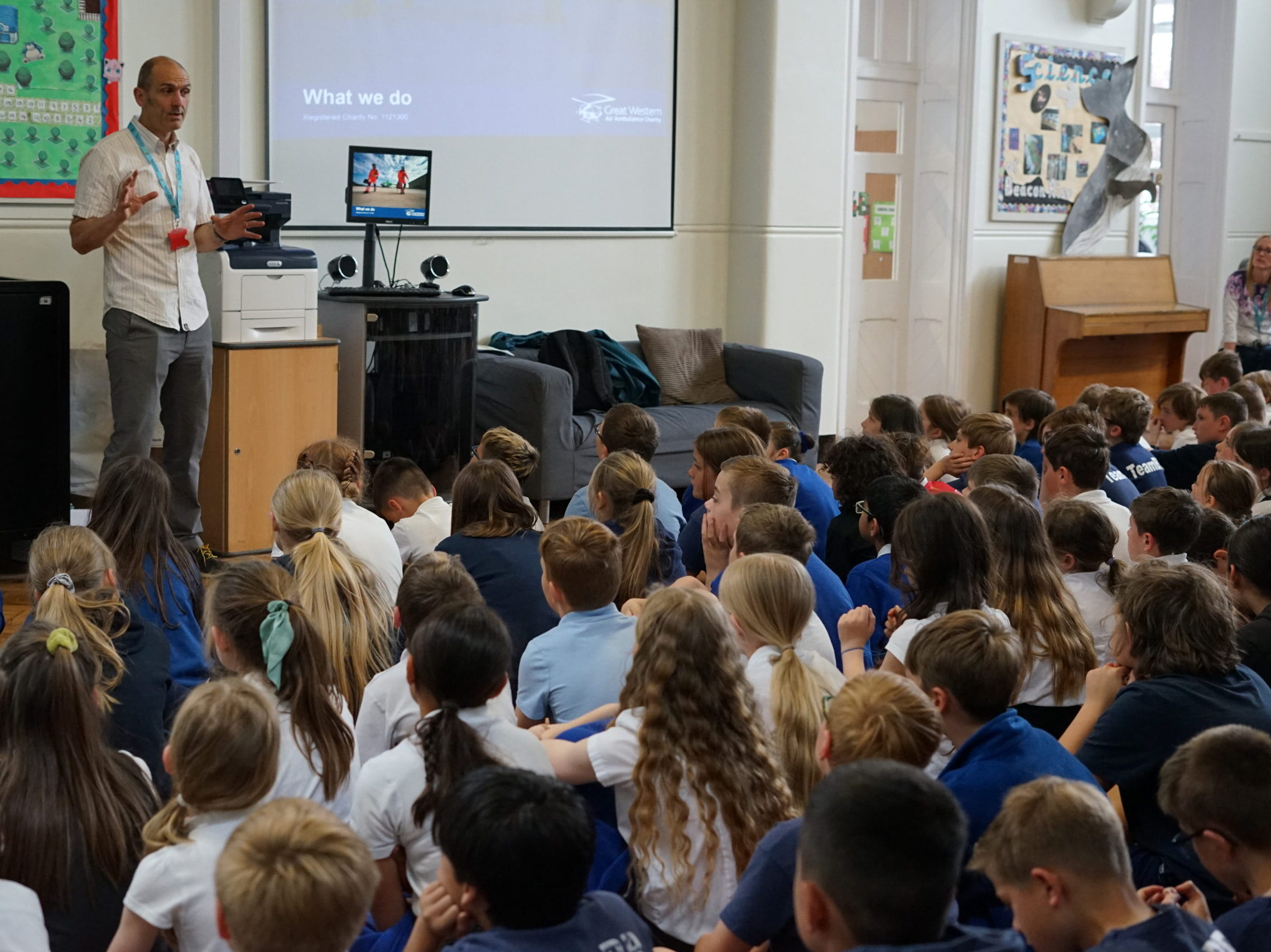 A volunteer with Charlie Bear doing a presentation to a hall full of schoolchildren