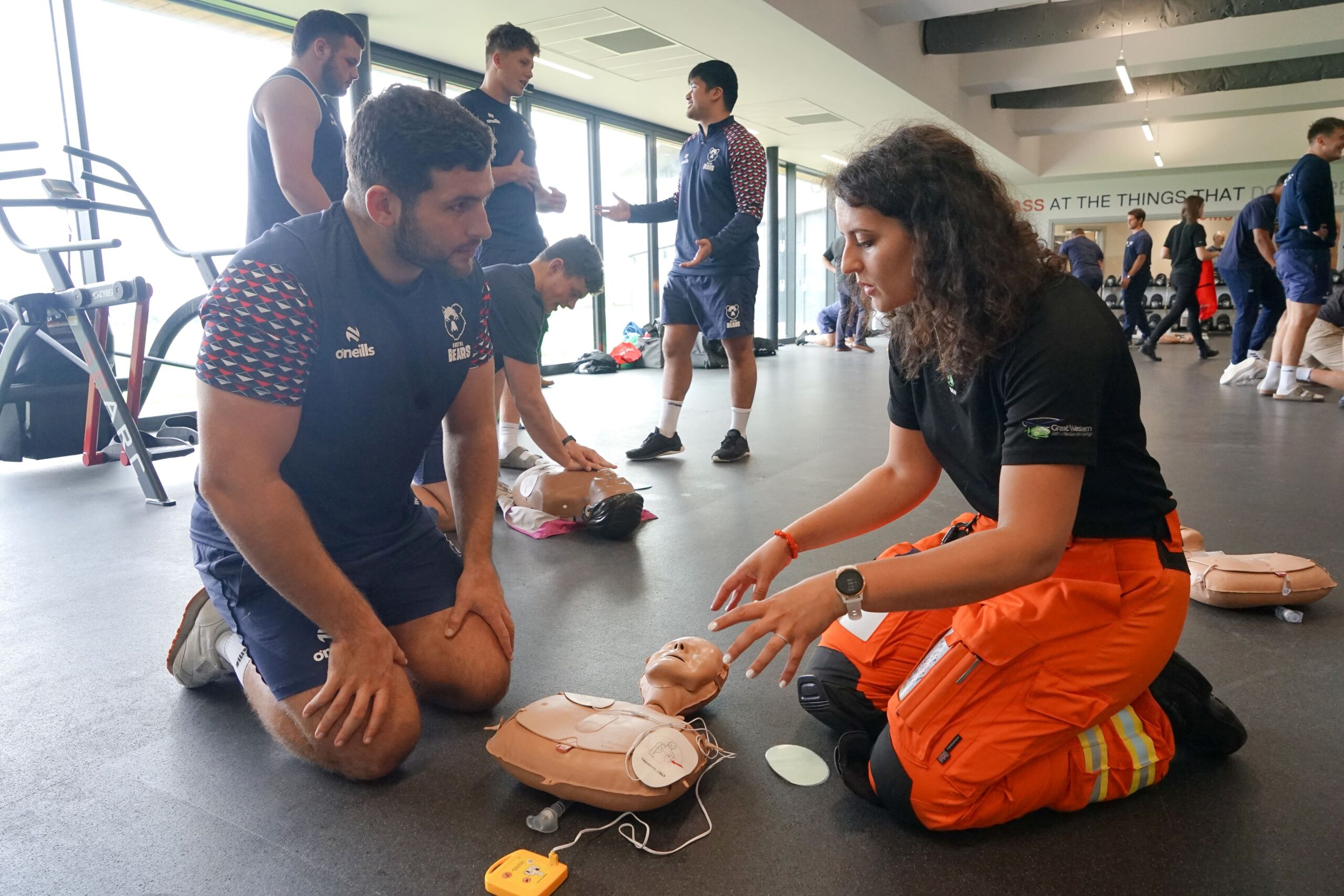 Specialist Paramedic in Critical Care Fleur Rath teaching a member of the Bristol Bears rugby team how to use an AED and do CPR at the Bristol Bears training ground