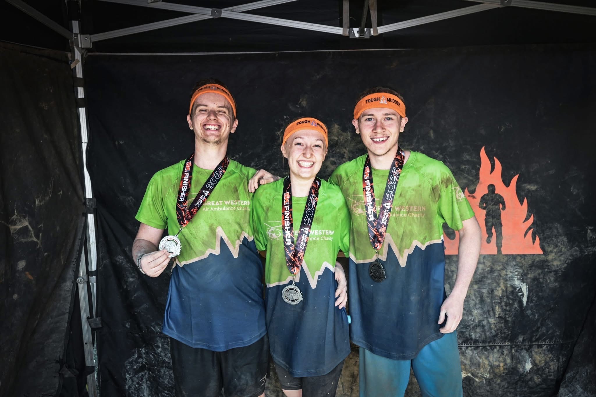 Emma, Tom and Nicholas pose with their medals whilst wearing very muddy green and blue GWAAC t-shirts