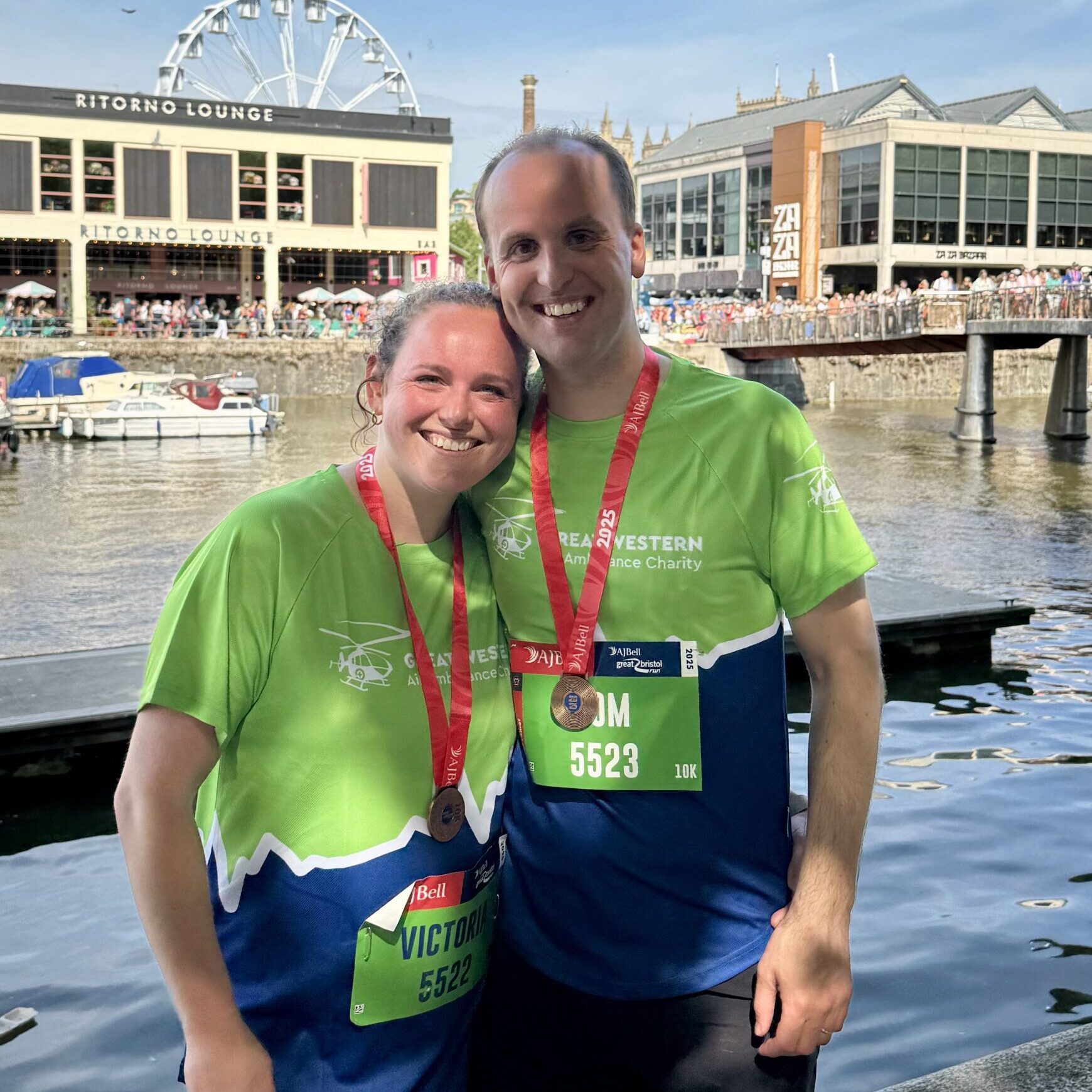A smiling Tom And Victoria in green and blue GWAAC running t-shirts wearing completion medals for The Great Bristol Run.