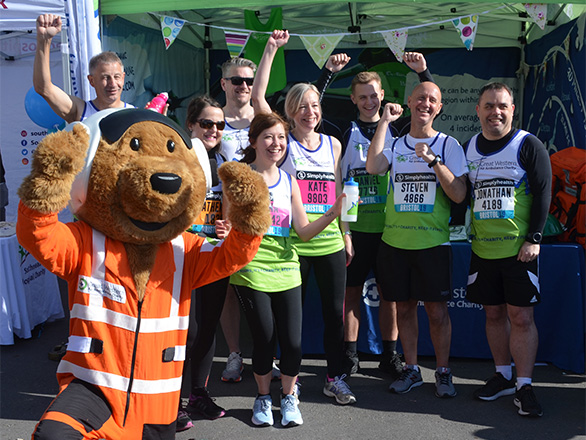 THe GWAAC mascot Charlie celebrating with a group of people in GWAAC running vests