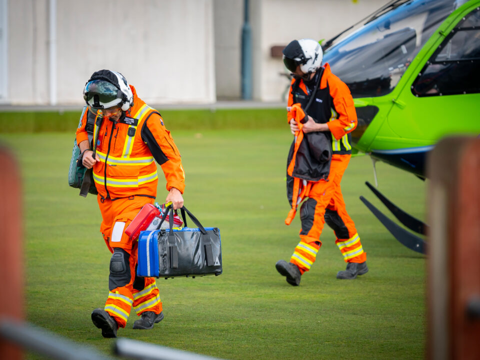 Two members of the GWAAC crew head from the green and blue helicopter with medical kit