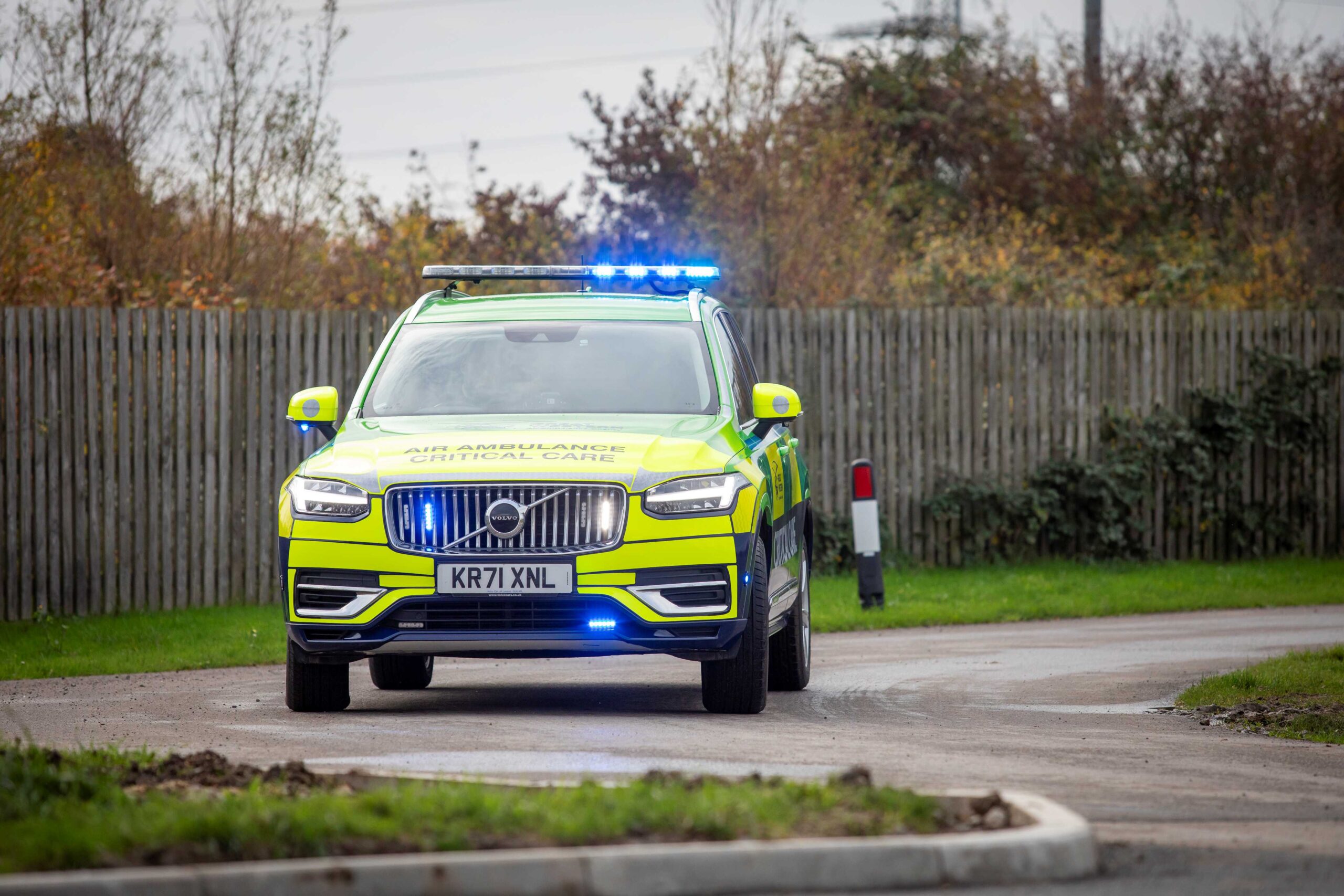 Great Western Air Ambulance Charity's new green, yellow and blue Volvo XC90 critical care car drives around a corner with it's blue emergency lights flashing