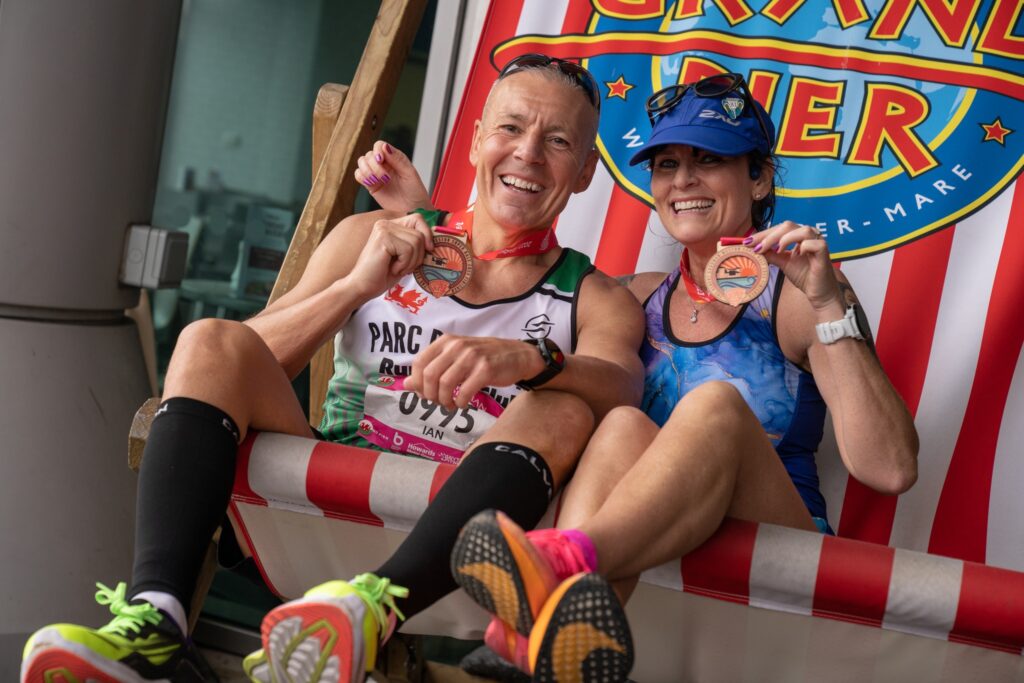 Two runners in a giant deckchair proudly showing off their finishers medals
