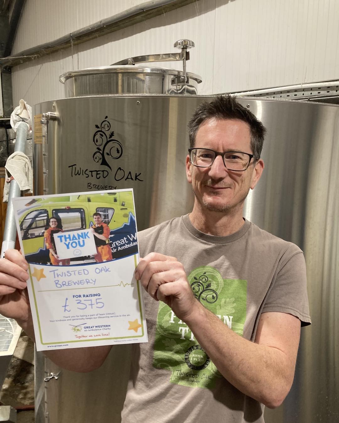 A member of the Twisted Oak Brewery team holds up a thank you certificate from GWAAC in front of brewing tank