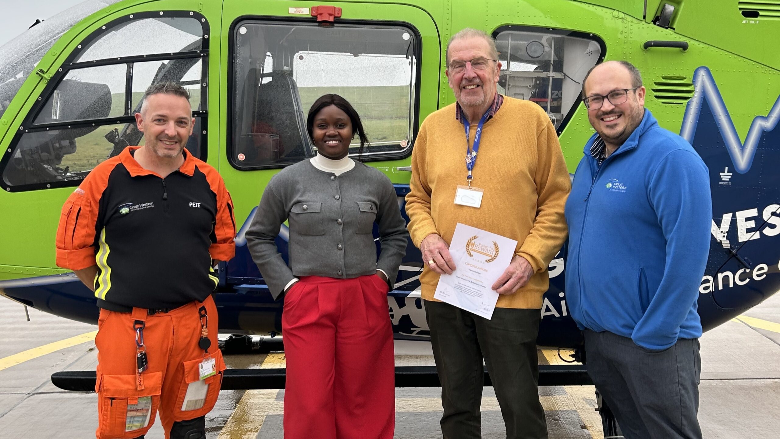 Steve poses with his certificate in front of the GWAAC green and blue helicopter, standing with GWAAC staff Dan and Caroline as well as Specialist Paramedic in Critical Care Pete