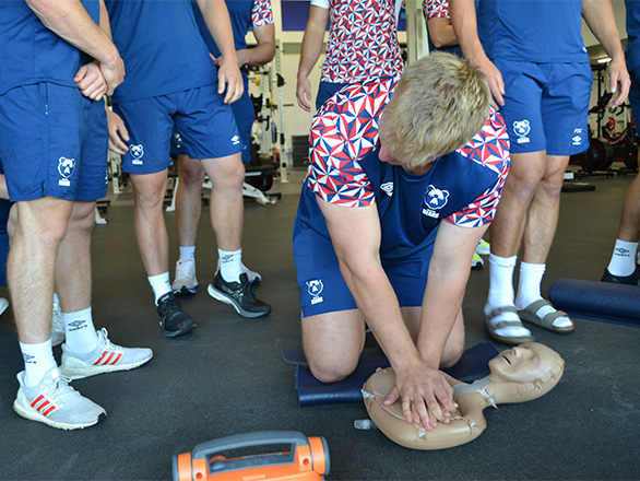 Someone in A Bristol BEars training kit practicing CPR on a training manikin