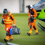 Two members of the GWAAC crew head from the green and blue helicopter with medical kit