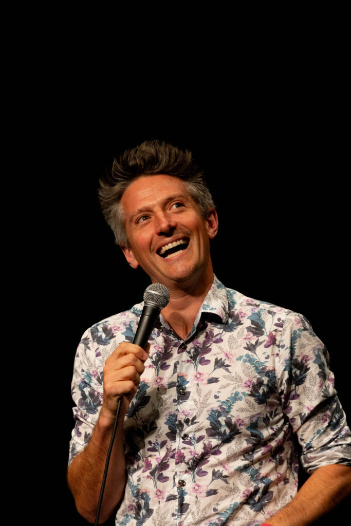 Comedian Stuart Goldsmith in a colourful shirt hosting Heli Laughs 2023 at The Old Vic Bristol