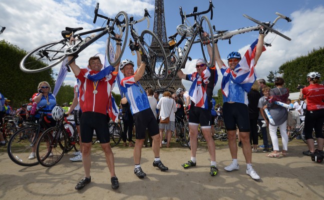 Cyclists holding bicycles aloft in front of the Eiffel Tower