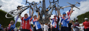 Cyclists adorned with Union Flags holding their bicycles aloft in front of the Eiffel Tower